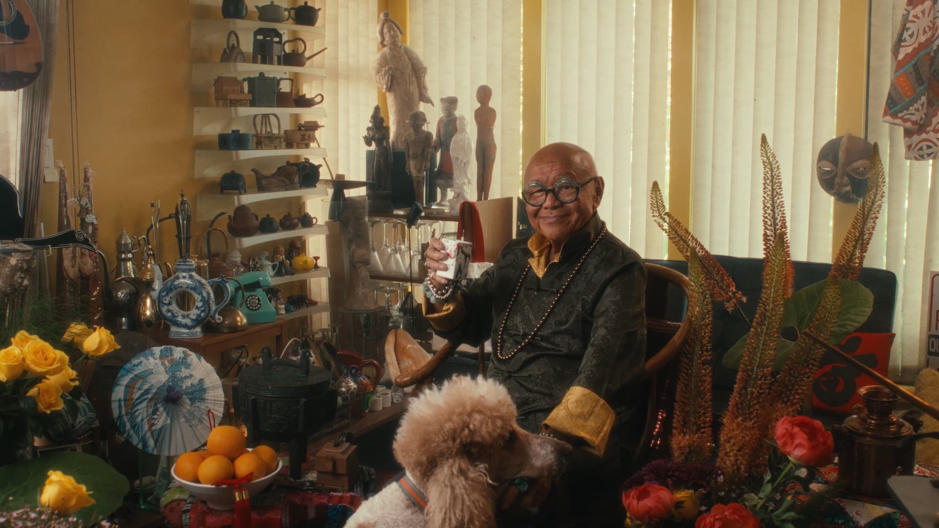 Roger Lee seated among artworks and flowers, still from the portrait film edited by Montreal video editor Victor Tamarit