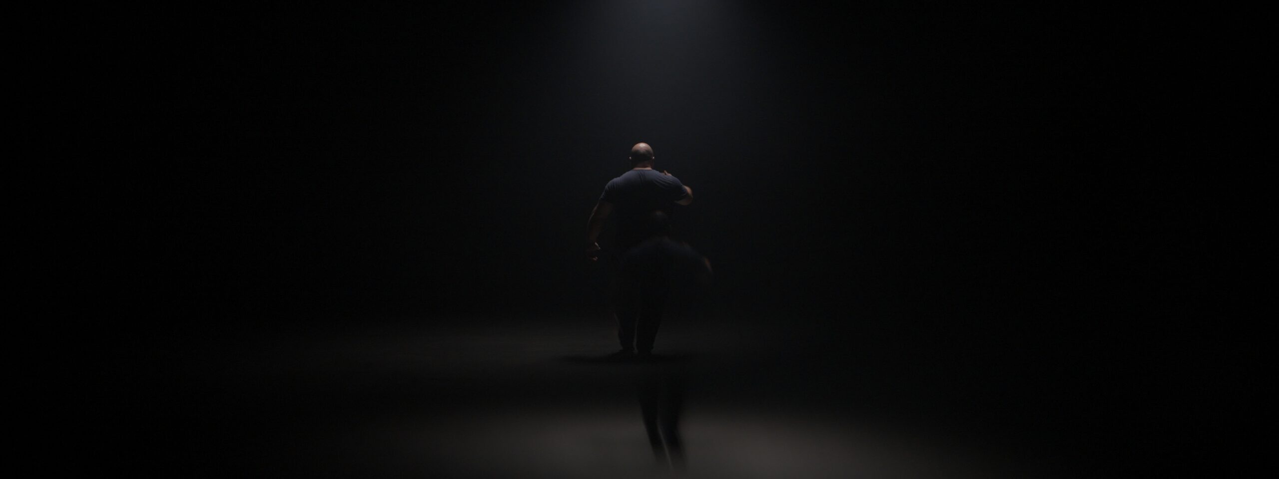 Lone figure under a single spotlight on a dark stage, film still from Montreal video editor Victor Tamarit